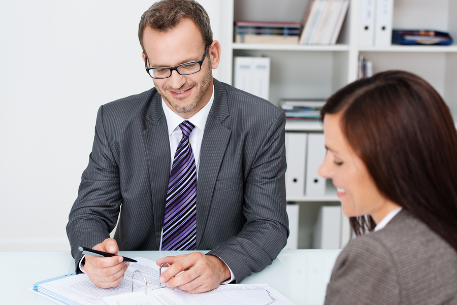 Business partners at work in the office with focus over the shoulder of a woman to a smiling confident businessman in glasses working on paperwork