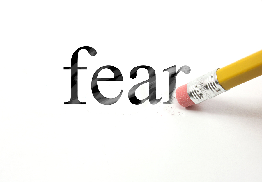The word Fear written with a pencil on white paper. An eraser from a pencil is starting to erase the word fear.