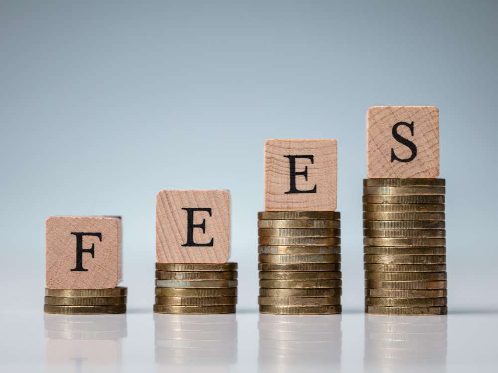 a stack of coins with blocks on top that spell the word "fees" to show increasing fees