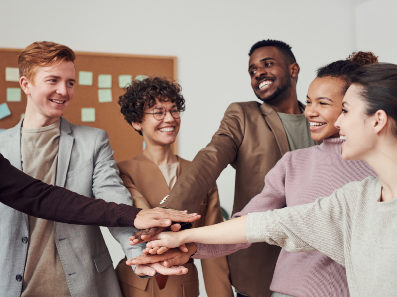 A diverse group of five smiling professionals stacking hands in a gesture of teamwork in recruitment business